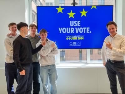 Fire elever og en mand peger på en skærm med teksten ' Use Your Vote'.