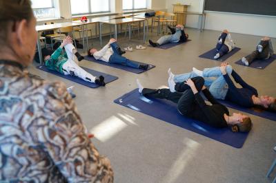 Eleverne ligger på yogamåtter i klasselokalet og lytter til læreren, der instruerer dem.
