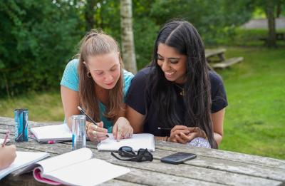 To piger laver matematik på en bænk udenfor skolen.