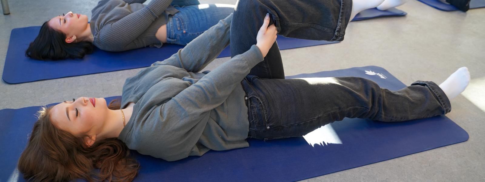 Fem elever laver liggende yoga på måtter i et klasselokale