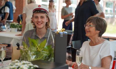 En smilende drengestudent sidder ved et bord i kantinen sammen med sin mor.