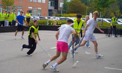 Elever spiller hockey på parkeringspladsen uden for skolen.