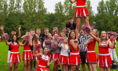 Cheerleaders poserer for kameraet. En pige bliver holdt oppe i luften af to andre piger.