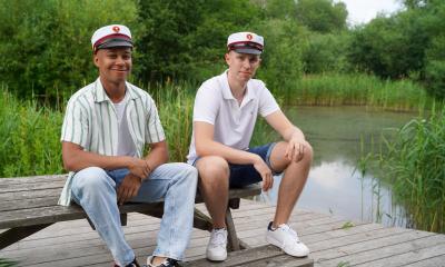To studenterdrenge sidder på en bænk ved søen uden for skolen.